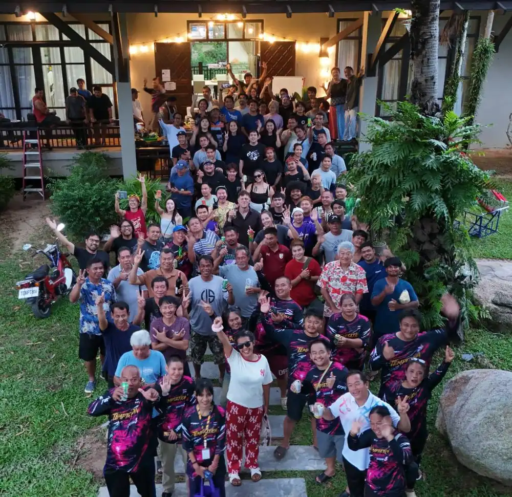 A drone view looking down on the full production unit, dozens of crew gathered on a lawn outside a house, waving up at the camera.