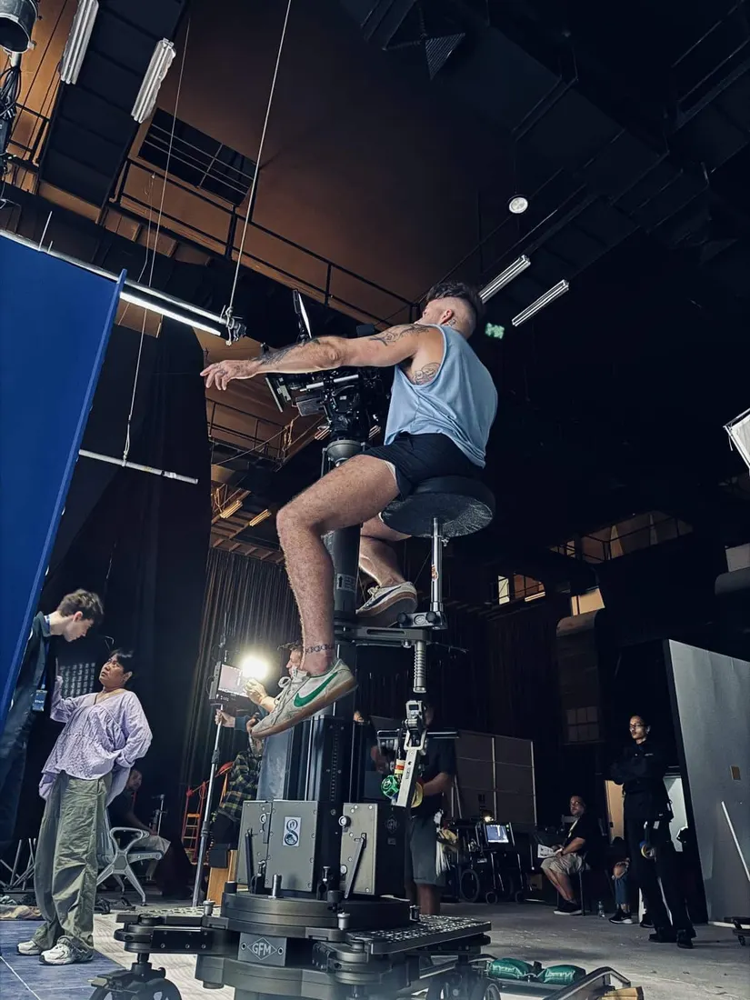 A camera operator perched on a motion control rig captures an action shot on a soundstage, with crew watching from below.