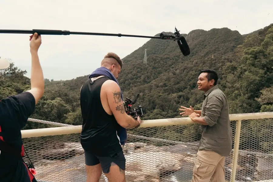 A boom operator and crew filming at a highland viewpoint.