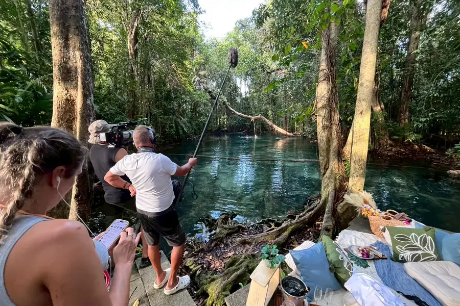 A boom operator and camera crew filming beside a jungle pool.