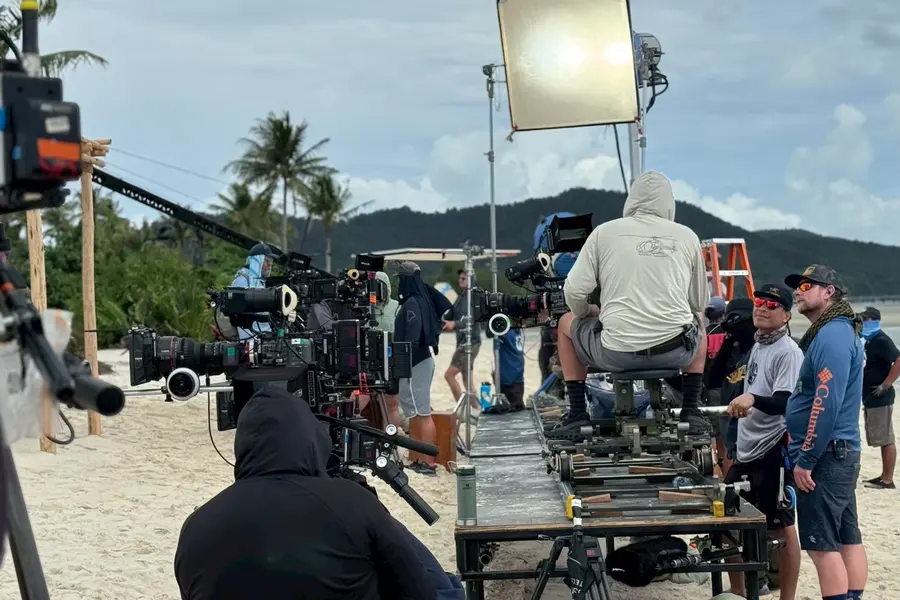 Camera crew working from a dolly track under a lighting unit on the beach.